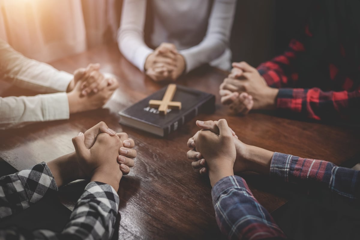 Grupo de cristianos tomados de las manos orando juntos con la Biblia sobre una mesa de madera