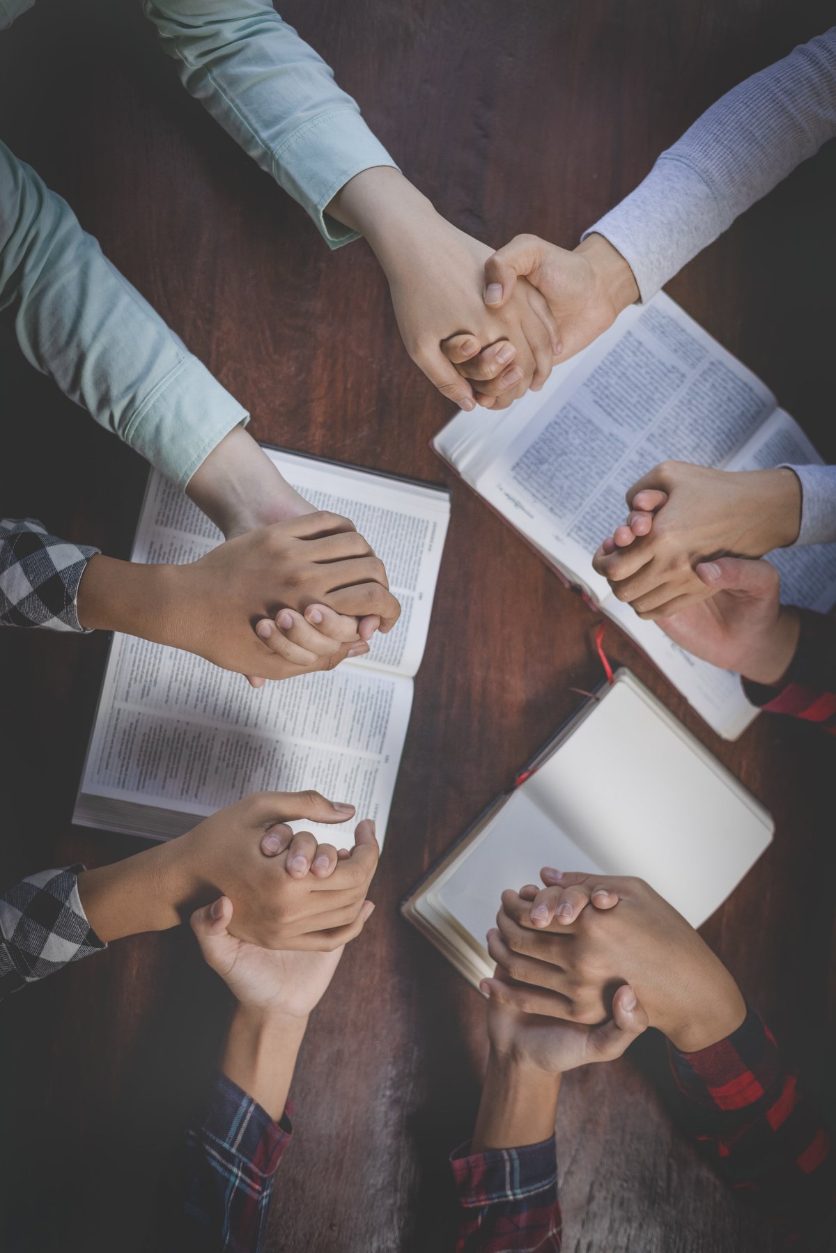 Grupo cristiano tomados de las manos orando con la Biblia